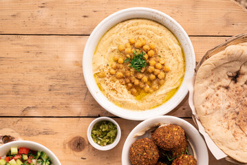 Israel traditional food hummus with chickpea and parsley, vegetarian falafel, pita, salad, fries and zhug on cozy wooden table outside. Top view.