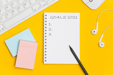 Text 2021 goals on notebook with pencil and office accessories on yellow background, office desk. Top view with copy space for input the text. 