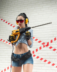 a slender woman in the image of a construction worker with a puncher against a white textured brick...