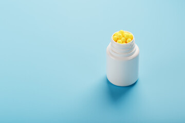 Vitamins of yellow color in the form of round dragees in a white jar on a blue background.