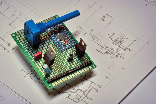 Prototype electronic circuit; DC motor control with elements such as a microcontroller, potentiometer, voltage regulator and FET deployed on PCB  over schematic hand-drawn circuit diagram on a paper.