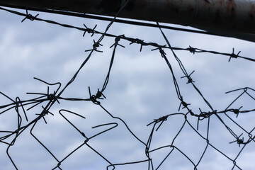 Metal barbed wire against an overcast blue sky in spring or winter and a hole in the fence. Protecting a parking lot, business or jail. 