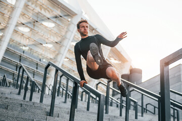 Does parkour. Young man in sportive clothes have workout outdoors at daytime