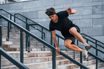 Fototapeta premium Jumps over obstacles. Young man in sportive clothes have workout outdoors at daytime