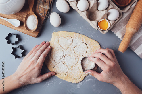 Girl prepares cookies in the shape of a heart, flat lay composition on a gray background. Cookie cutters and dough in women's hands. Concept of food for Valentine's Day, Father's Day, Mother's Day