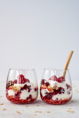 Two glasses of yogurt, oat flakes and raspberries with wooden spoon standing together