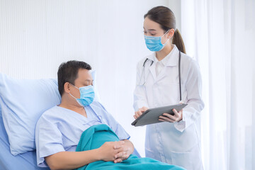 Obraz premium Asian woman doctor talking with a man patient who he is on bed about his pain and symptom in hospital. They wear a medical face mask to protect respiration system (Covid-19).