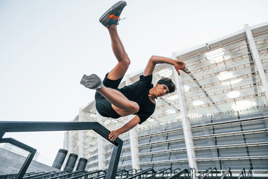 Does parkour. Young man in sportive clothes have workout outdoors at daytime