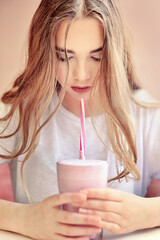 Beautiful girl with a glass cup of delicious fragrant pink Milkshake drinks with a straw in her hands with her head bowed