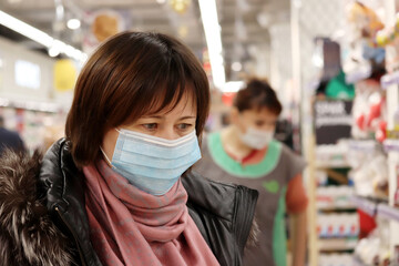 Woman in warm clothes and medical mask choosing products in a supermarket. Concept of safety during shopping at coronavirus pandemic