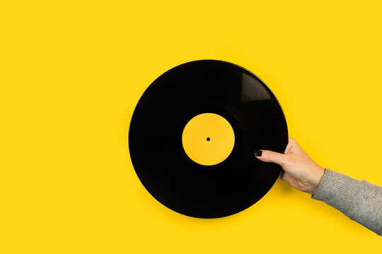 Mano de mujer sosteniendo un disco de vinilo sobre un fondo amarillo liso y aislado. Vista de frente. Copy space