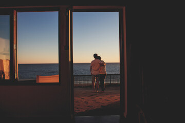 young couple arm in arm looking out on the ocean during sunset