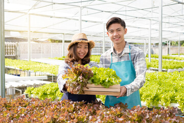 Hydroponics, smiling young Asian couple farmers holding vegetable baskets, standing on a farm, growing organic, commercial organic vegetables. Organic farming business concept