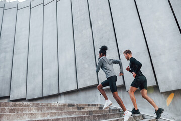 Near big wall. European man and african american woman in sportive clothes have workout together