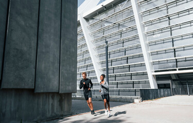 Near big wall. European man and african american woman in sportive clothes have workout together