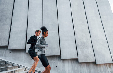 Near big wall. European man and african american woman in sportive clothes have workout together
