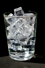 Transparent ice cubes are in a transparent glass on a black background.