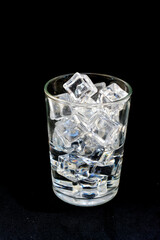 Transparent ice cubes are in a transparent glass on a black background.