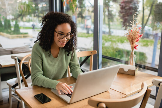 African American freelancer in glasses using laptop in cafe