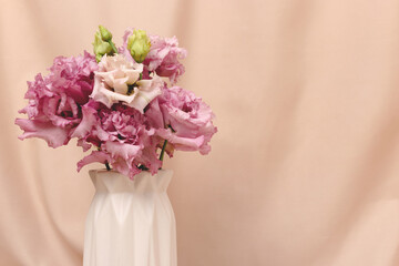 Bouquet of eustoma flowers in vase in front of beige cloth background. Surprise for Womans or Mothers Day. Springtime concept with copyspace.
