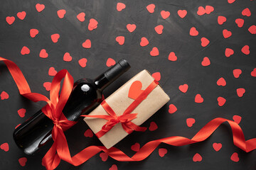 A bottle of wine near the packed box. Valentine's Day. On a concrete background with paper hearts.