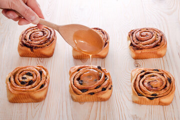 Freshly baked sweet bun with raisins and cinnamon on wooden table. Glazing a Cinnabons won. Homemade traditional bakery, baking bread and sweets concept.