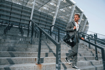 Young businessman in grey formal wear is outdoors in the city