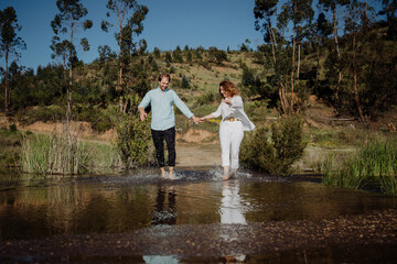 Fototapeta premium Couple running through the water, splashing each other. Welcoming the spring. Springtime