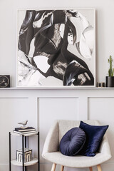Stylish interior of living room with design grey armchair, pillows, marble stool, paintings, cacti, decoration, black clock and elegant personal accessories in modern home decor.