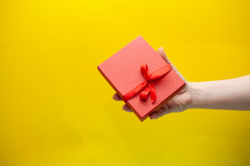 Woman's hand holding red gift box on yellow background