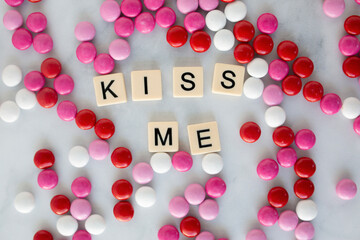 the words kiss me written in scrabble tiles on a marble kitchen counter top surrounded by valentines candy