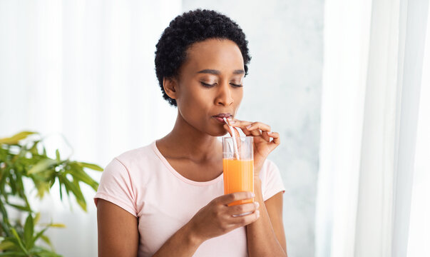 Pretty black woman drinking fresh orange juice at home, panorama
