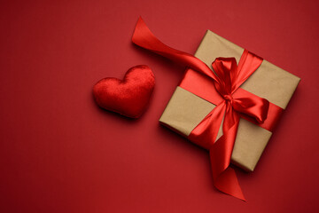 square box with red silk bow and textile heart  on red background, top view