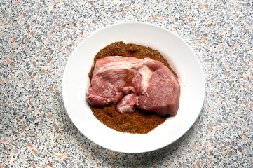 A piece of spiced meat in a plate before frying