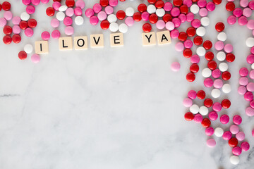 the words i love ya written in scrabble tiles on a marble kitchen counter top surrounded by valentines candy