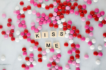 the words kiss me written in scrabble tiles on a marble kitchen counter top surrounded by valentines candy