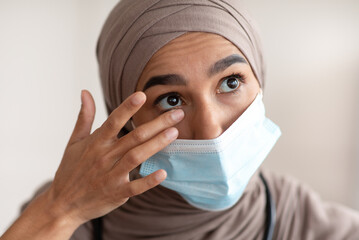 Overworked female doctor in hijab touching her eyes