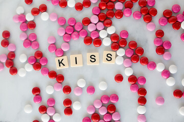 the word kiss written in scrabble tiles on a marble kitchen counter top surrounded by valentines candy
