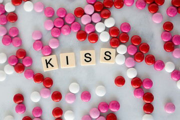 the word kiss written in scrabble tiles on a marble kitchen counter top surrounded by valentines candy