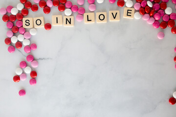 the words so in love  written in scrabble tiles on a marble kitchen counter top surrounded by valentines candy