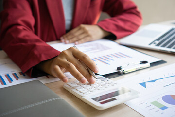 Female finance workers are using a calculator to calculate the company's earnings from a bar graph. That show the profit of the company At her desk in the office