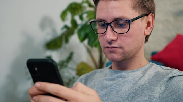 Young man sits on bean bag and urf the internet using a mobile phone, staying isolated at home. Having fun.