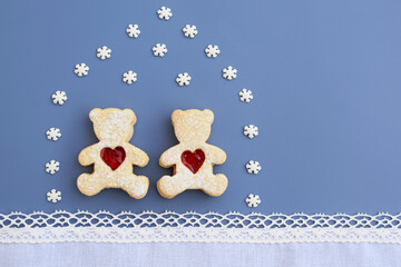 Creative romantic concept - linzer cookies in a shape of bears with heart in a house created from small sugar snowflakes. Blue background, white lacy border. Greeting card, copy space for text