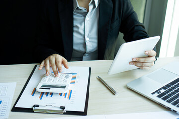 ..Female finance workers are using a calculator to calculate the company's earnings from a bar graph. That show the profit of the company At her desk in the office
