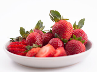 A fresh served plate of whole and sliced strawberries isolated on a white background