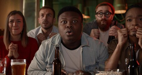 Group of young people become sad while watching sports game on TV. Diverse friends looking dissapointed while sitting at table with beer and supporting team. Concept of lose
