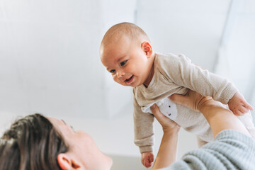 Young mother having fun with cute baby boy on hands in bright room love emotion