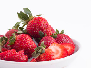 A fresh served plate of whole and sliced strawberries isolated on a white background