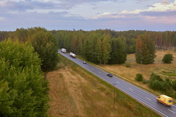 Cars on a rural asphalt road next to forest in summertime