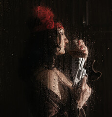 woman with a revolver in her hands and a glass behind a wet glass with raindrops